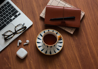 Laptop, cup of tea, notebook, glasses, headphones on a wooden table, top view