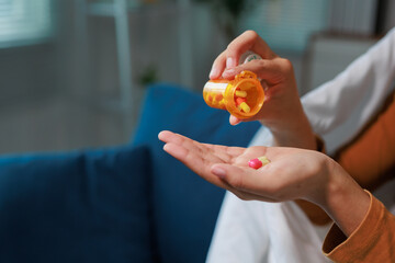 Patient resting on a sofa at home, pouring colorful pills from an orange prescription medication...