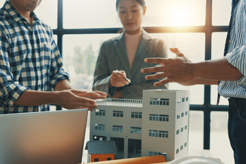 Architects and engineers collaborating over a building model during a meeting in the office,...