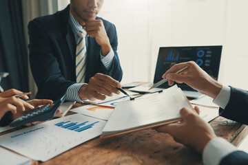 Business people are analyzing financial data and working with documents during a meeting, using a...
