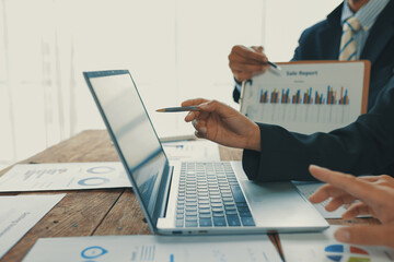 Business colleagues are reviewing financial reports on a laptop and printed documents, pointing at...