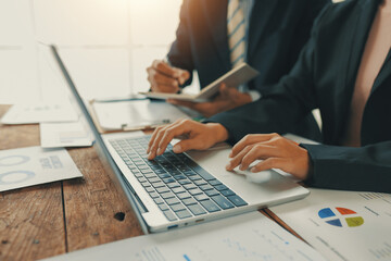 Business team working together on wooden table, analyzing financial statistics displayed on laptop...