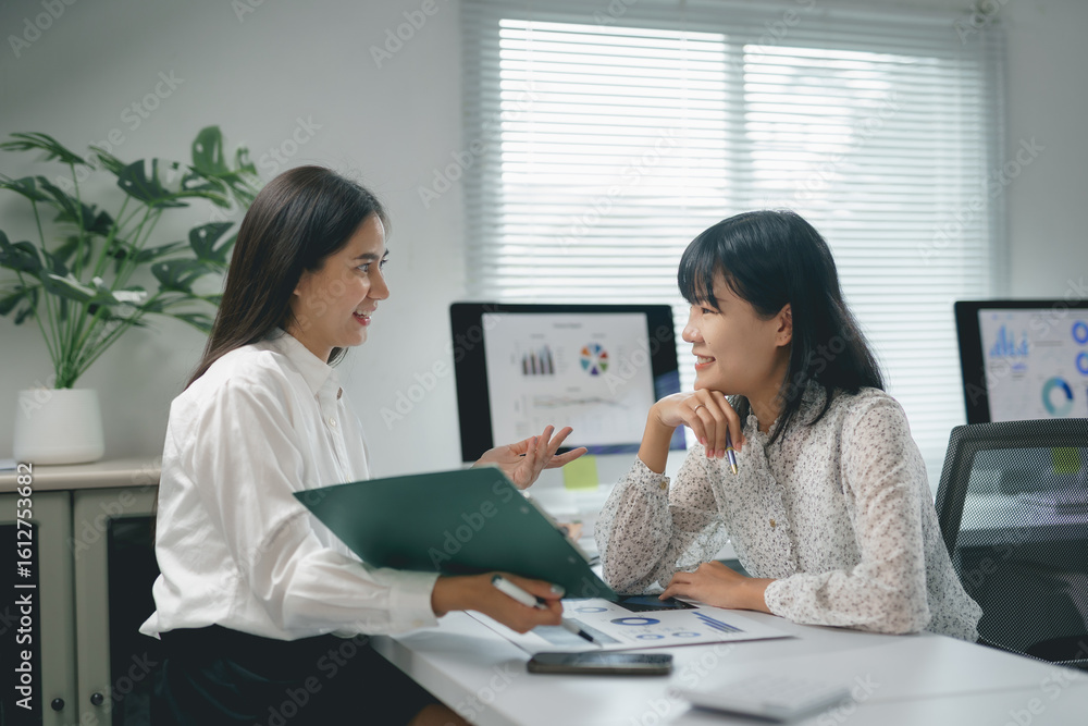 Poster two asian businesswomen are discussing financial data in a bright modern office, collaborating on a 