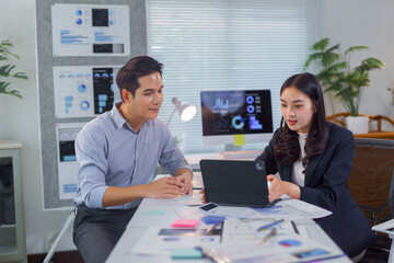 Two asian businesspeople are discussing statistics using a laptop in a modern office, collaborating on a project and analyzing data displayed on the screen