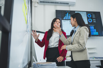 Two asian businesswomen discussing marketing strategy using whiteboard and interactive display...