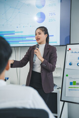 Asian businesswoman leads a presentation using a microphone. Gesturing with her hand and explaining...