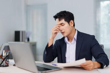 Young businessman suffering from headache or eyestrain after long computer work at modern office....