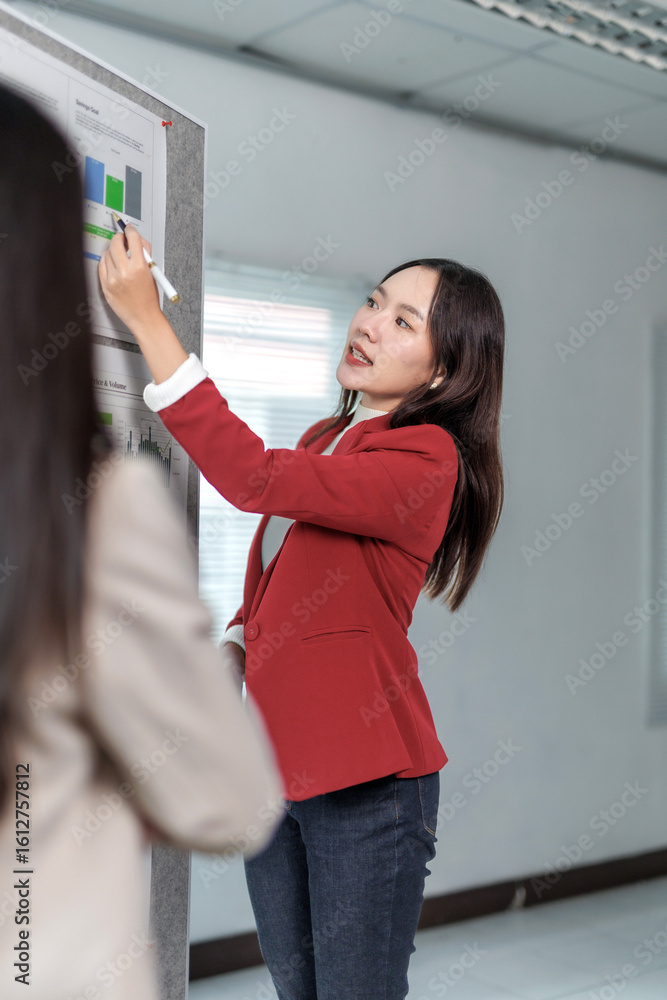 Poster young professional woman pointing at whiteboard using a marker and explaining charts and graphs to h