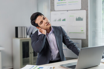 Young businessman suffering from neck pain while working on a laptop in the office, he is massaging...