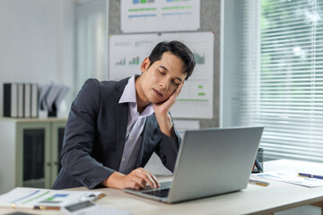 Young manager dozing off at workplace with hand on cheek, struggling to stay awake in front of computer, experiencing fatigue and burnout from overwork