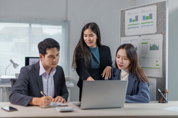 Three asian businesspeople are working together using a laptop in an office meeting, analyzing...
