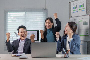 Euphoric businesspeople celebrating a successful project, raising their arms in excitement while...