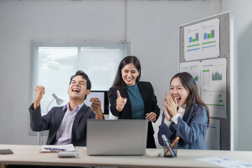 Euphoric businesspeople celebrating company success in the office, raising arms in joy while...