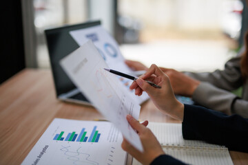 Two businesswomen are discussing company performance, pointing at financial charts and graphs...