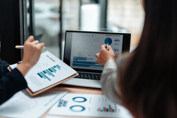 Two businesswomen are having a meeting analyzing financial charts and graphs displayed on a laptop...