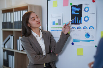 Businesswoman using pen pointing at charts and graphs on whiteboard, explaining diagrams and...