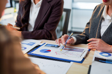 Businesswomen pointing at financial charts and graphs while discussing company performance,...