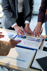 Businesswomen pointing at financial charts and graphs while discussing company performance and...