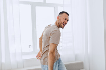 Joyful man smiling while dancing near a window, showcasing a vibrant atmosphere with bright, soft...