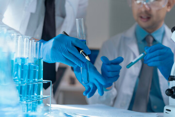 Two medical researchers wearing gloves are comparing and analyzing a test tube containing a blue...
