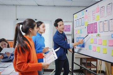 Young Asian businessman pointing at the whiteboard and presenting mobile application layout...