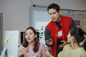 Three Asian coworkers engaging in a project discussion while collaborating over a computer in a...