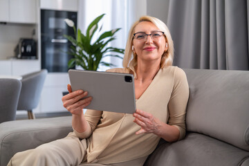 Blonde woman watching a show or movie on her digital tablet, enjoying quiet time in her living room. Technology and relaxation.