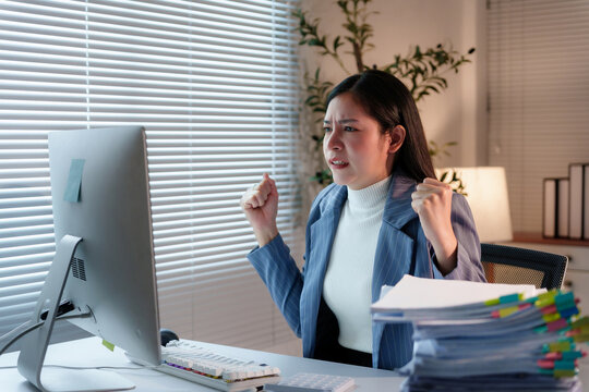 Young professional woman working in office is overwhelmed by workload and is showing frustration and anger while looking at desktop computer - Powered by Adobe