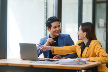 Two asian businesspeople are discussing and working together, using a laptop computer in the...