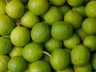 close-up of fresh green limes piled together, showcasing their vibrant color and textured skin,...