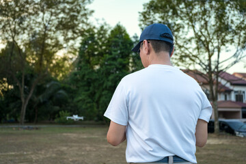 Man operating drone in the field with a controller. Back view of man. 