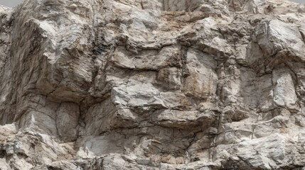 Rugged granite cliff reveals intricate textures and natural formations against a cloudy sky. The scene highlights the geological features found in mountainous terrain during afternoon light.