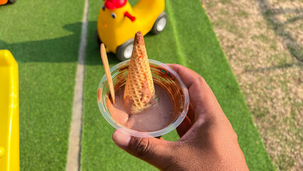 hand holding melting ice cream in a plastic container with a playground background