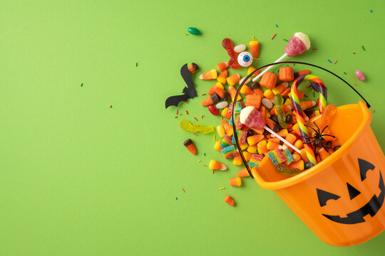 An orange Halloween bucket spills vibrant candies and decorations on a green backdrop