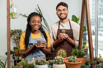 Young man and woman selling cactuses in a flower shop and looking happy