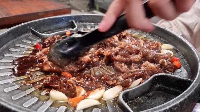 Footage captures the moment enoki mushrooms are placed onto a hot Korean BBQ grill loaded with marinated meat, garlic, chili, and onions