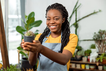Young cute african american woman holding a pot with cactus and smiling