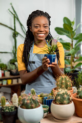Young cute african american woman holding a pot with cactus and smiling