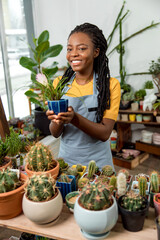 Young cute african american woman holding a pot with cactus and smiling