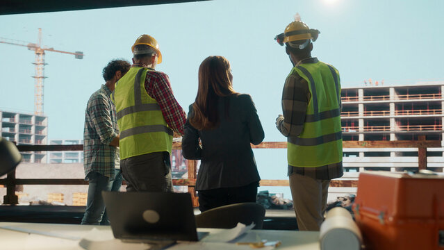 Diverse team of architects and engineers observing construction progress from office window