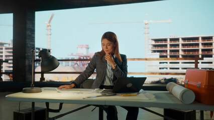 Female architect reviewing blueprints in office overlooking construction site