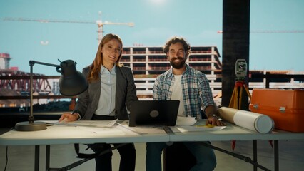 Smiling architects presenting project sitting at desk in construction site office during the day