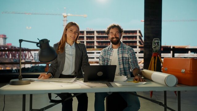 Smiling architects presenting project sitting at desk in construction site office during the day