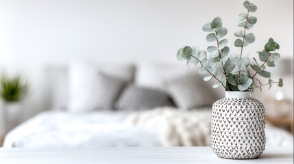 A potted eucalyptus plant in a patterned vase on a white surface.
