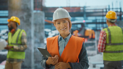 Smiling female chief engineer holding tablet computer and working on construction site