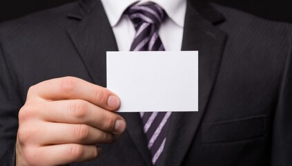 Formal suited man holding a blank white card with a dark tie. The background is black, drawing attention to the crispness of the shirt and professional attire