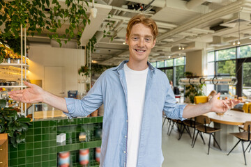 Ginger young guy in blue tshirt welcoming clients in a cafe