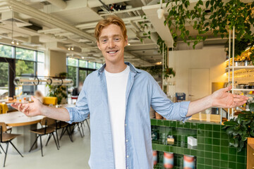 Ginger young guy in blue tshirt welcoming clients in a cafe