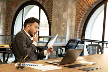 Young businessman scrutinizing document and looking concentrated