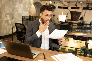 Young businessman scrutinizing document and looking concentrated